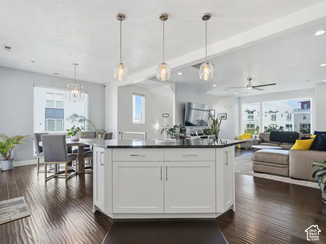 Kitchen island with white shaker-style cabinetry, dark stone countertop, three brushed-nickel glass pendant lights, and wood-finish flooring