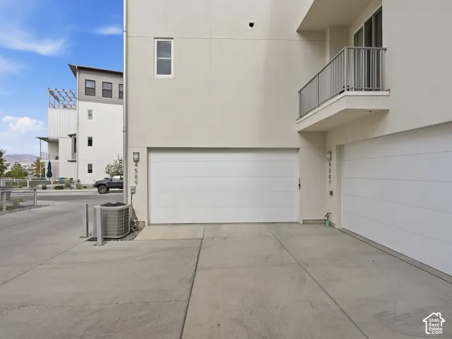 Contemporary exterior featuring light-toned smooth siding, a private balcony with metal railings, and dual individual garage bays with paved driveway access