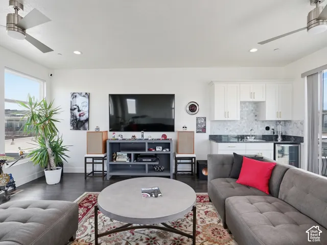 Living area featuring wood-finish flooring, dual brushed-nickel ceiling fans, recessed lighting, and a wet bar with white shaker-style cabinetry, stone-composite countertops, and a tiled backsplash