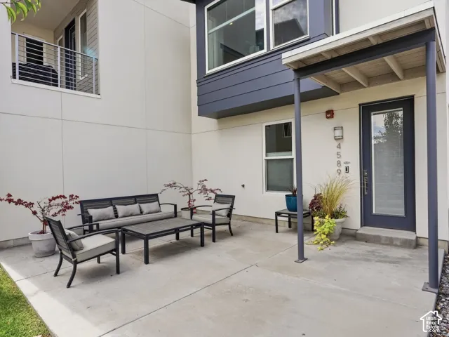 Concrete patio with a covered entrance featuring a steel-frame canopy, exterior metal sconce lighting, and a metal-trimmed glass-panel door