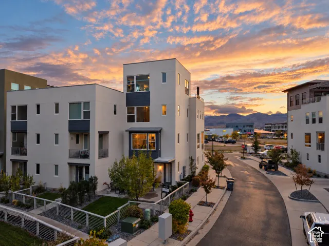 Modern multi-story structure featuring smooth stucco siding, large vertical windows, private balconies with metal railings, and a mountain backdrop