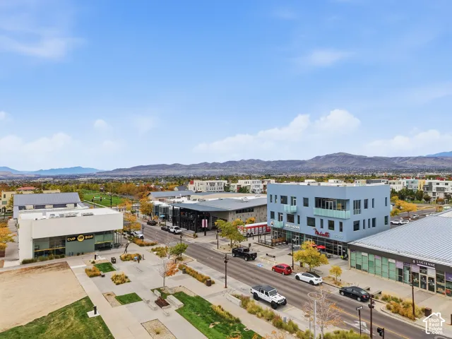 Aerial perspective of a multi-building urban complex featuring contemporary multi-story structures, paved pedestrian walkways, manicured landscaping, and distant mountain backdrops