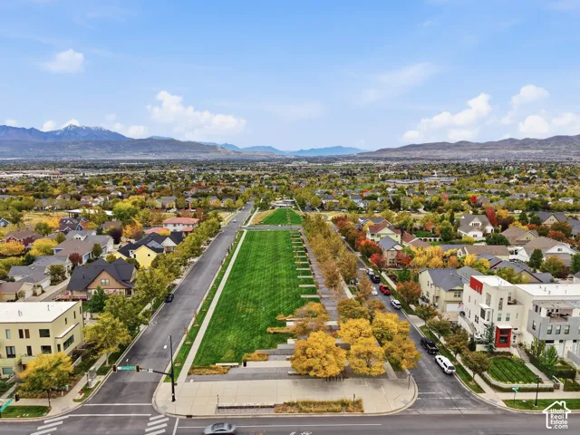 Aerial perspective featuring an elongated central greenbelt, manicured landscaping, mature trees, and a mountain range backdrop