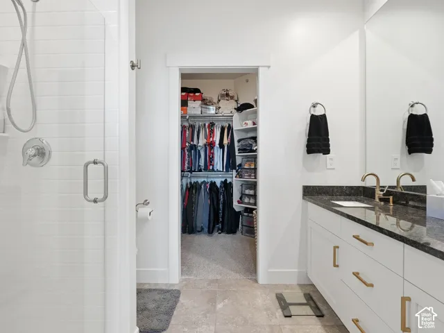 Bathroom featuring a walk-in shower with white subway tile, a white vanity with gold-tone hardware and stone countertop, large wall-mounted mirror, and a walk-in closet with built-in shelving