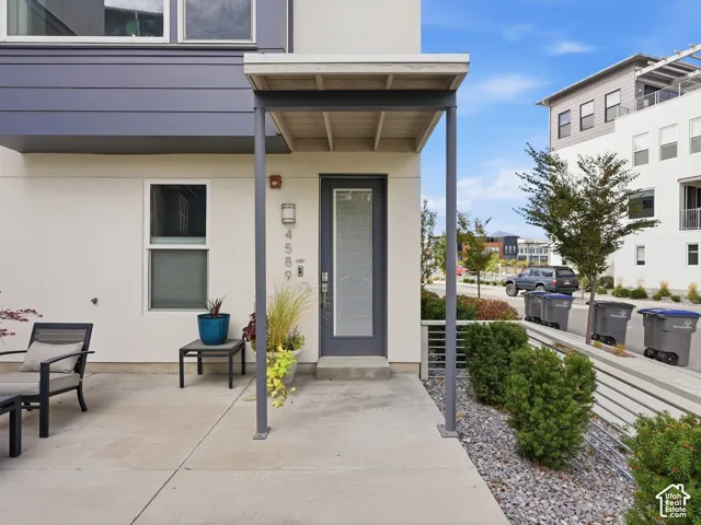 Modern exterior featuring smooth stucco siding, dark metal trim, a covered entryway with a minimalist support column, and a concrete patio