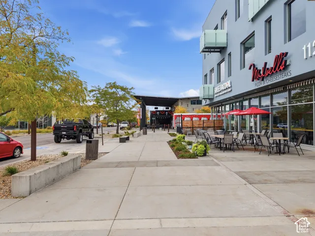 Modern commercial building featuring expansive glass storefronts, concrete pedestrian walkways, cantilevered balcony structures, and integrated landscaping