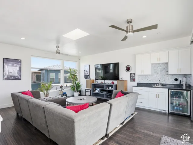 Open living area featuring wood-finish flooring, a built-in wet bar with white cabinetry and dark countertops, a recessed skylight, and dual ceiling fans