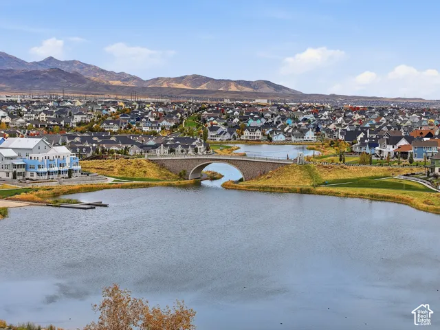 Aerial perspective of a lakefront community featuring a stone-arch bridge, expansive waterfront, paved walking paths, and mountain scenery