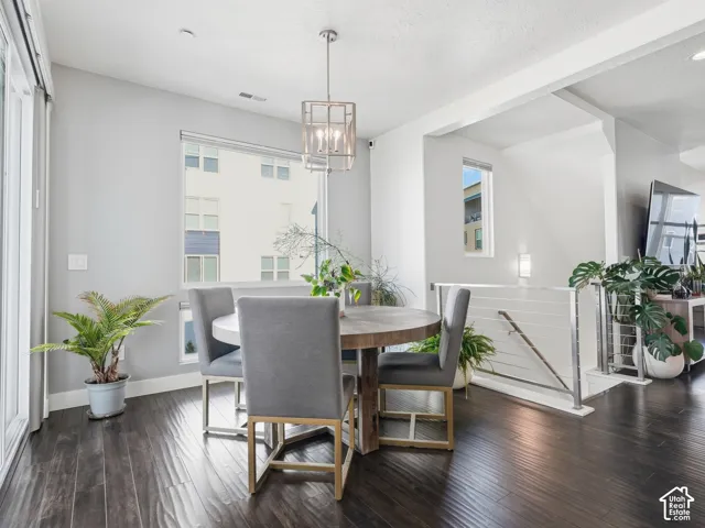 Dining area featuring dark wood-finish flooring, a metallic geometric pendant light fixture, large picture windows, and a metal cable railing system