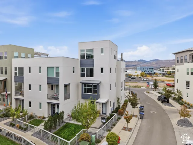 Multi-level architectural exterior with a light stucco finish, charcoal metal paneling accents, recessed balconies, and horizontal metal railing enclosures