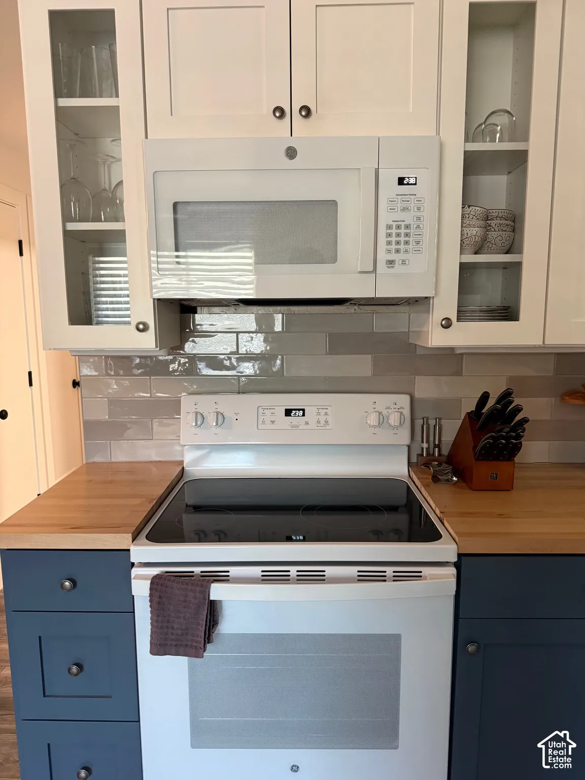 Shaker-style cabinetry, glossy subway tile backsplash, butcher block countertops, white over-the-range microwave, and white electric range