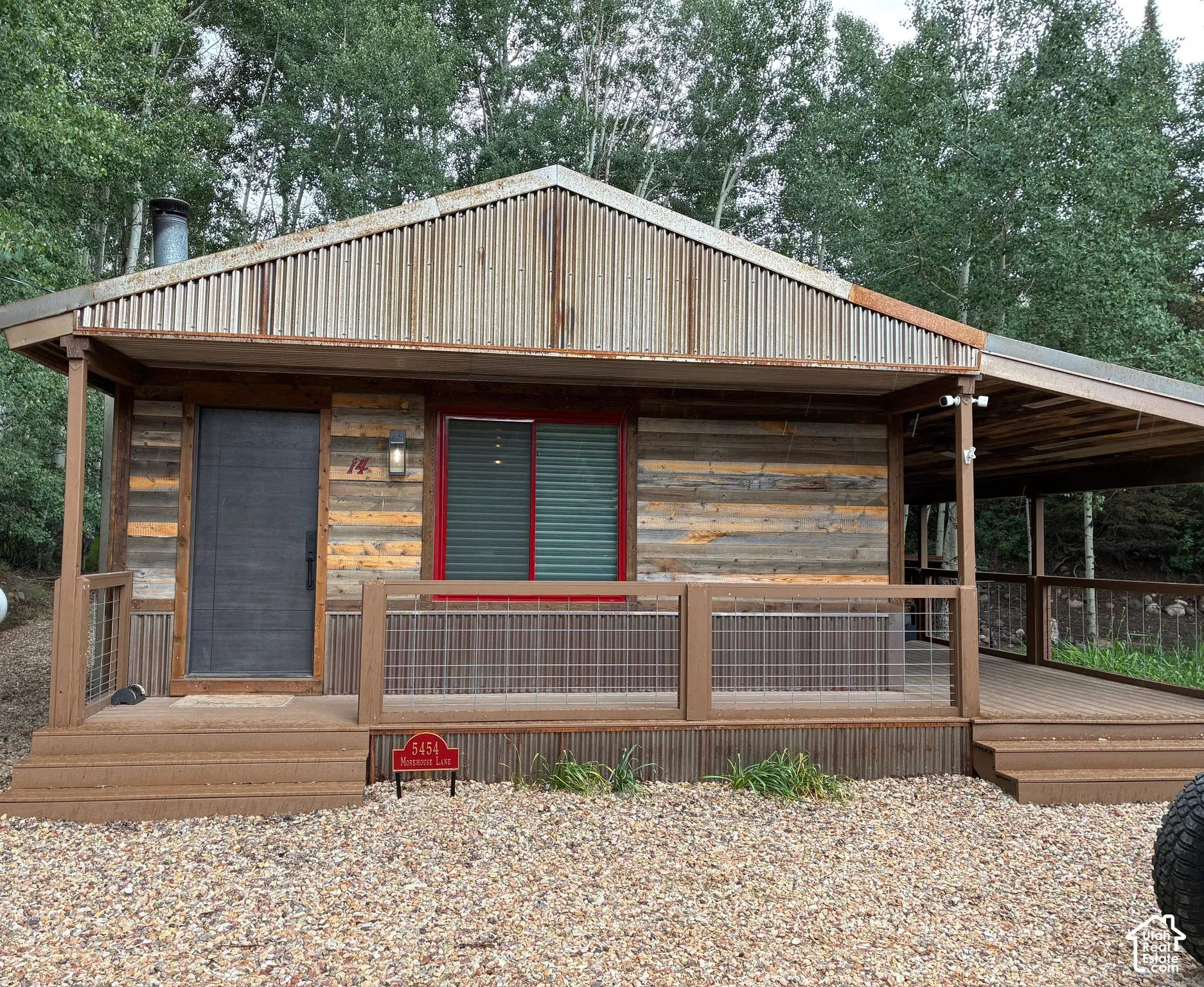 Exterior featuring reclaimed wood siding, corrugated metal roofing, a wide covered porch, wire railing, and a gravel ground surface