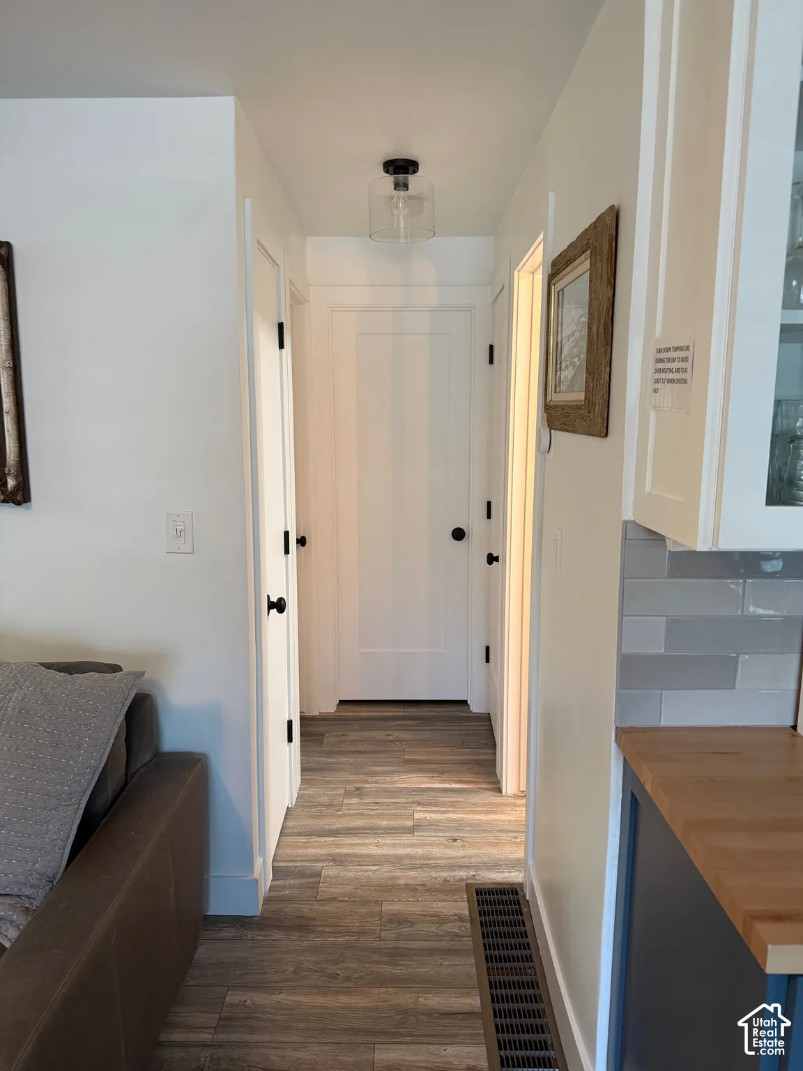 Interior hallway featuring wood-finish flooring, shaker-style interior doors with matte black hardware, and a glass-shade flush mount light fixture