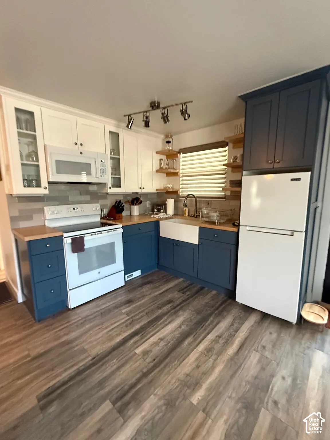 Kitchen featuring dual-tone cabinetry, wood-finish flooring, a farmhouse-style apron sink, butcher block countertops, and a tiled backsplash