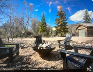 Gravel grounds featuring a metal fire pit, mature evergreen trees, and a detached structure with wood-finish siding
