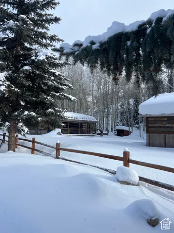 Exterior grounds featuring mature evergreen trees, a wooden rail fence, and a rustic log structure