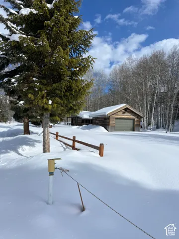 Wood-sided structure with a gabled roof and detached garage, featuring post-and-rail fencing amidst mature pine and aspen trees