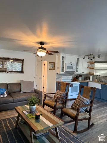 Wood-finish flooring, kitchen cabinetry with glass-front accents, farm-style sink, and integrated ceiling fan with light fixture