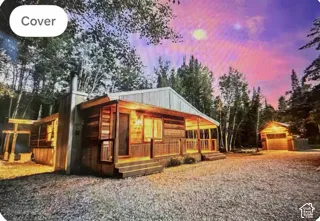 Rustic log exterior featuring a covered front porch, vertical wood siding, exterior chimney, and detached garage situated on a gravel lot