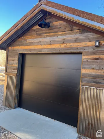Exterior featuring reclaimed wood siding, corrugated metal wainscoting, a flat-panel garage door, and a black gooseneck exterior wall light