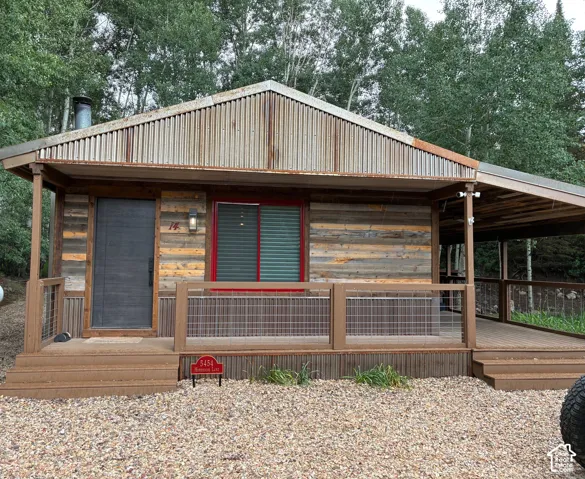 Exterior featuring reclaimed wood siding, corrugated metal roofing, a wide covered porch, wire railing, and a gravel ground surface
