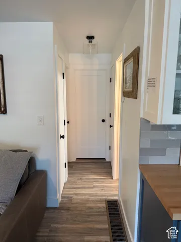 Interior hallway featuring wood-finish flooring, shaker-style interior doors with matte black hardware, and a glass-shade flush mount light fixture