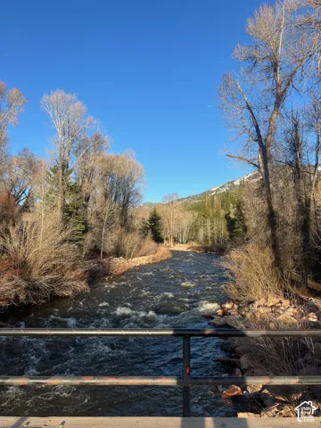 Waterfront property bordering a mountain-fed stream with a metal guardrail, rock-lined banks, and mature native trees