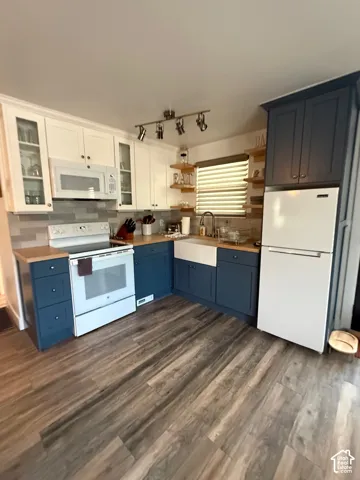 Kitchen featuring dual-tone cabinetry, wood-finish flooring, a farmhouse-style apron sink, butcher block countertops, and a tiled backsplash