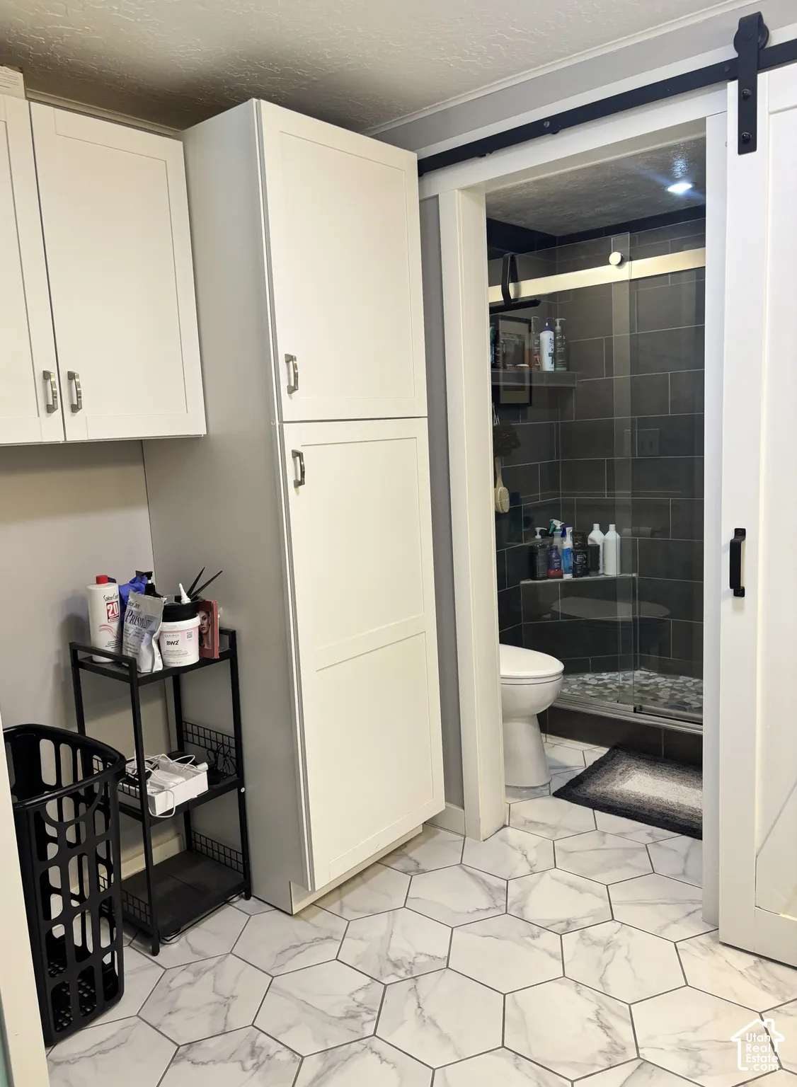 White cabinetry with silver-tone hardware, white-and-grey hexagonal floor tile, sliding barn door with black hardware, and tiled shower enclosure