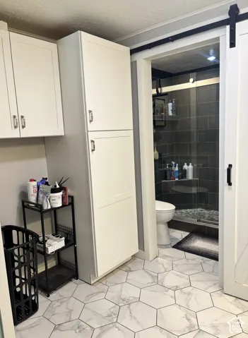 White cabinetry with silver-tone hardware, white-and-grey hexagonal floor tile, sliding barn door with black hardware, and tiled shower enclosure