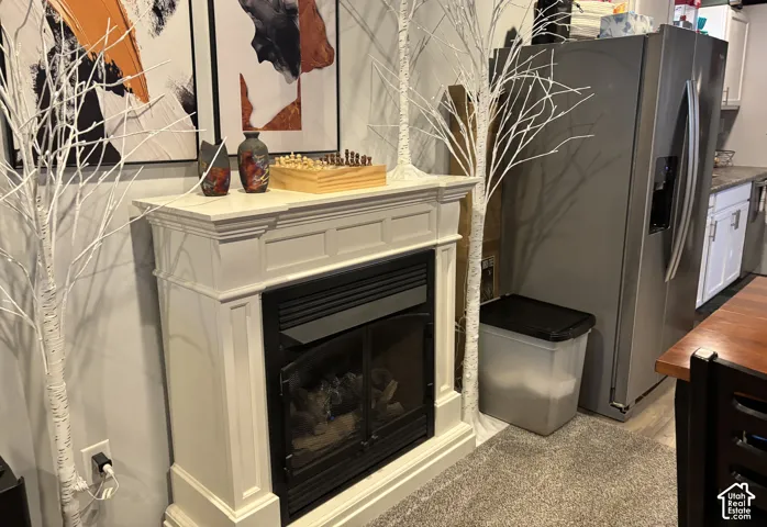 Custom-built white wood-finish fireplace mantel with classic paneling detail, glass-front hearth, stainless steel side-by-side refrigerator, and white cabinetry
