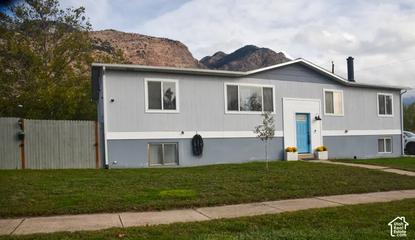 Two-tone exterior siding featuring a painted entry door, concrete walkway, enclosed perimeter fencing, and mountain backdrop