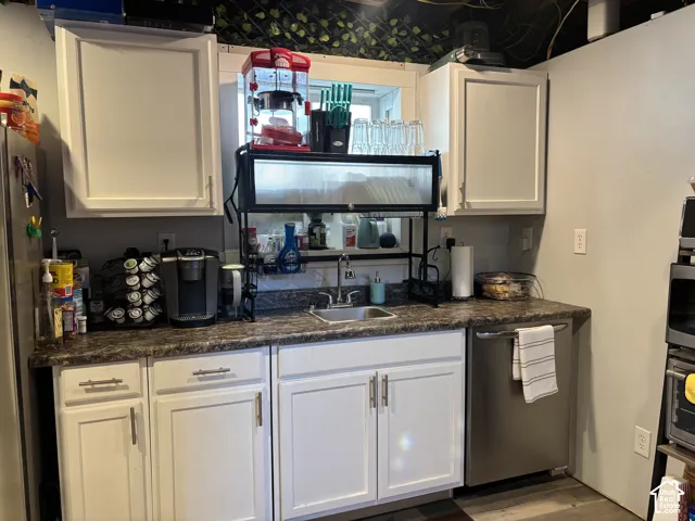 White shaker-style cabinetry, high-contrast dark laminate countertops, stainless steel undermount sink, and stainless steel dishwasher