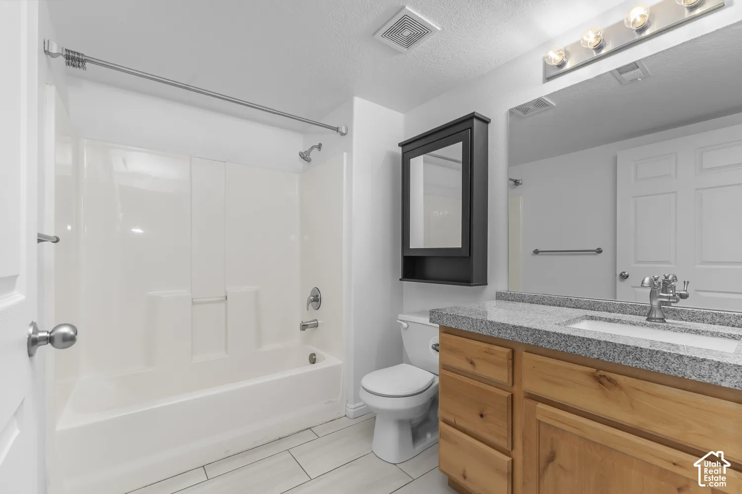 Bathroom featuring a vanity with wood-finish cabinetry, a speckled countertop, an integrated sink, a wall-mounted medicine cabinet, and a tub-shower combination with a surround