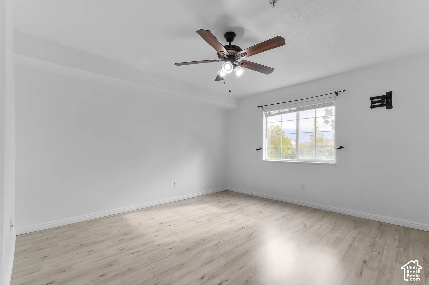 Light-filled room featuring wood-finish flooring, a ceiling fan with integrated lighting, and a window with exterior mullions