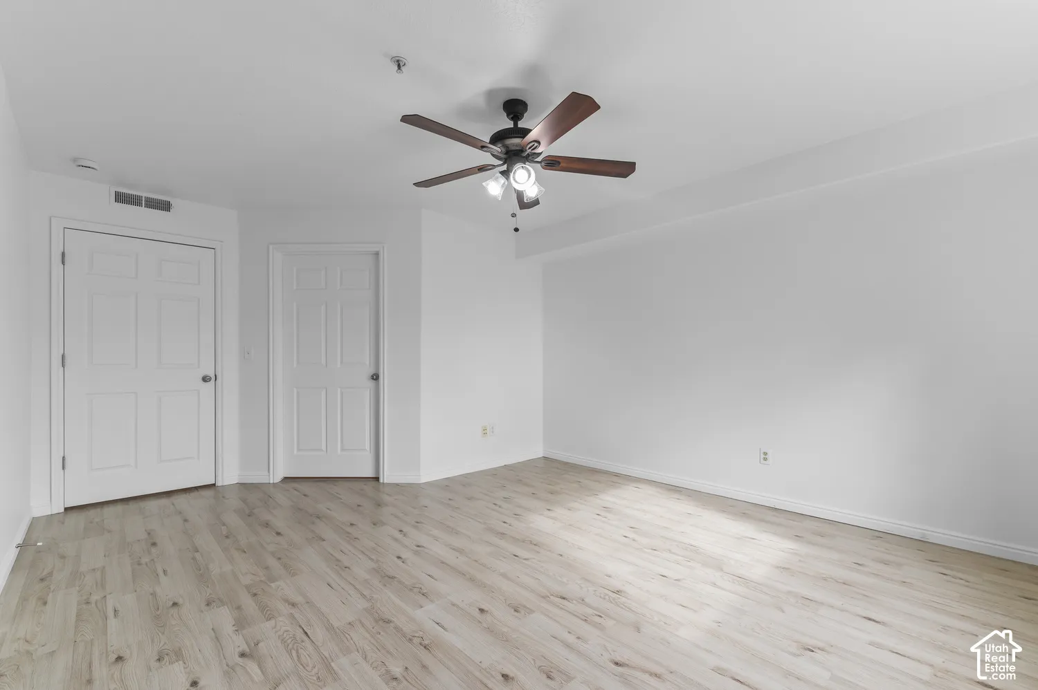 Interior room featuring light wood-finish flooring, white walls, and a ceiling-mounted fan with integrated lighting fixtures