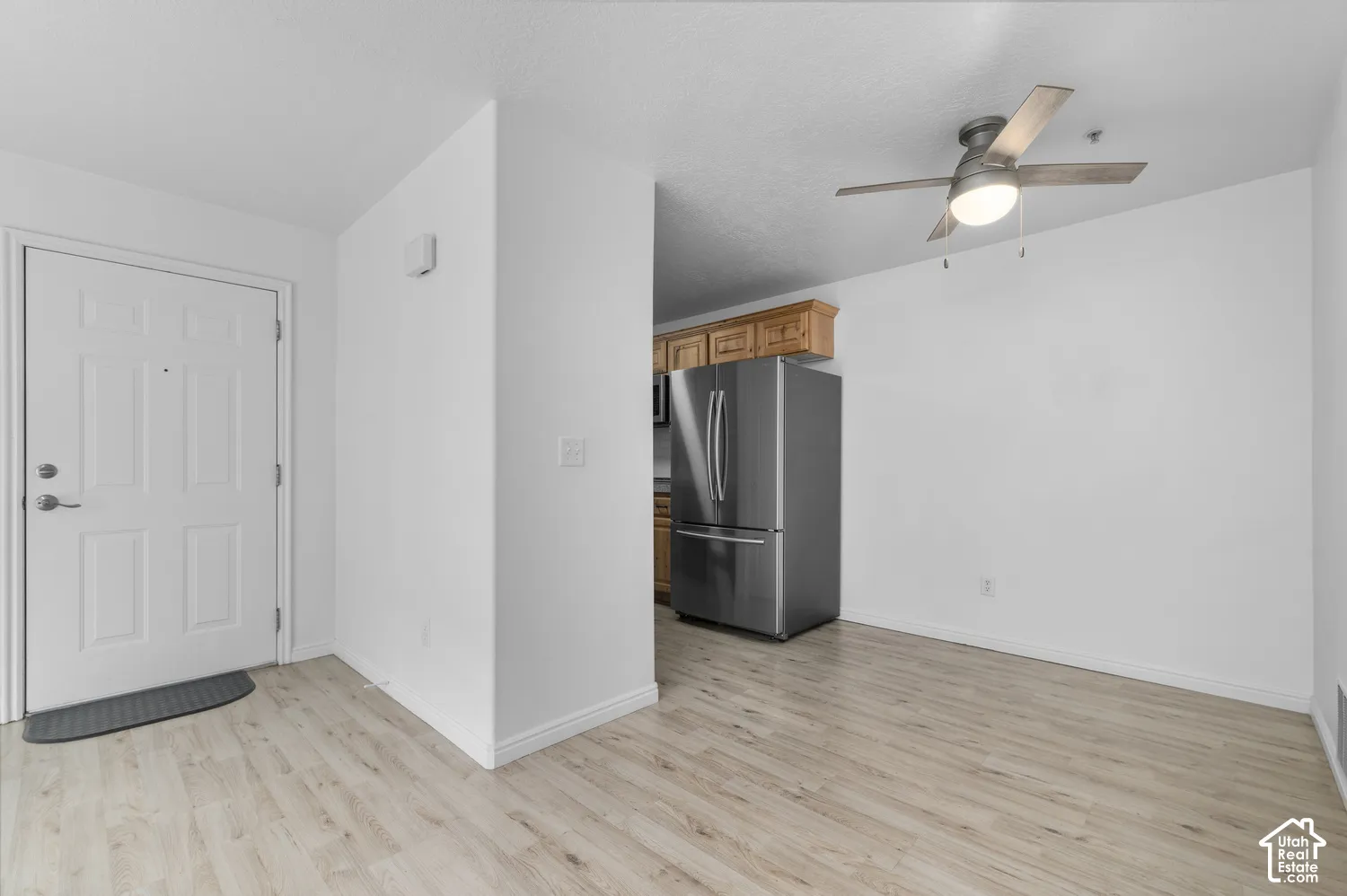 Entryway featuring wood-finish flooring, ceiling fan with integrated lighting, stainless steel refrigerator, and wood-finish cabinetry