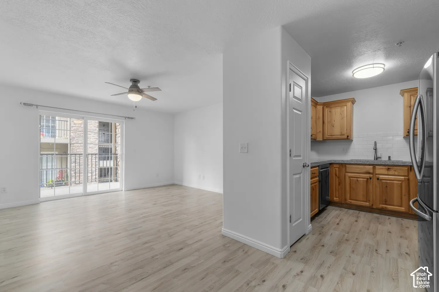 Kitchen featuring wood cabinetry, stone countertops, and tile backsplash, accompanied by a living area with wood-finish flooring, a ceiling fan, and sliding glass doors leading to a balcony