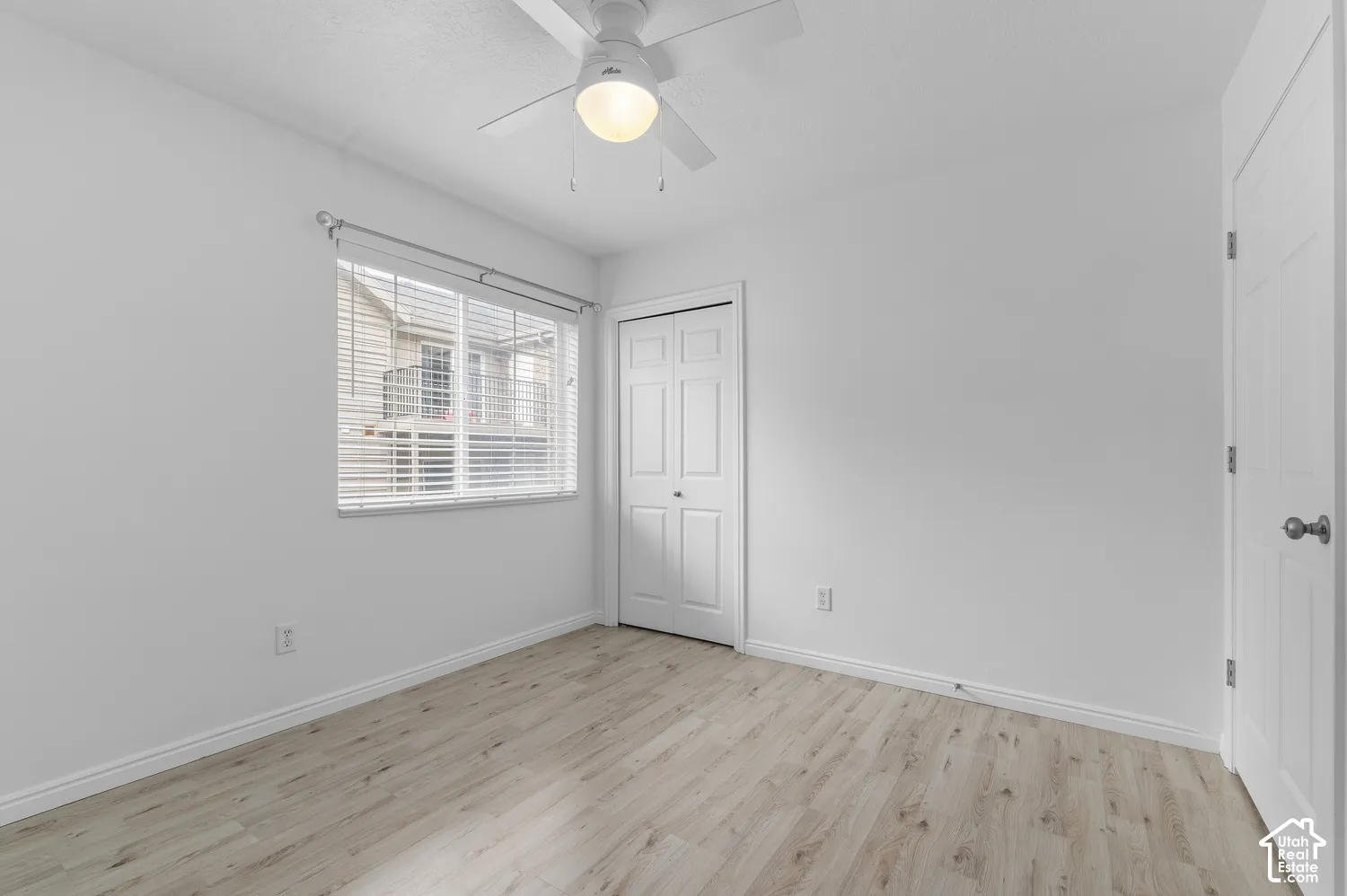 Neutral-toned wood-finish flooring, ceiling fan with integrated light fixture, horizontal window blinds, and paneled closet doors