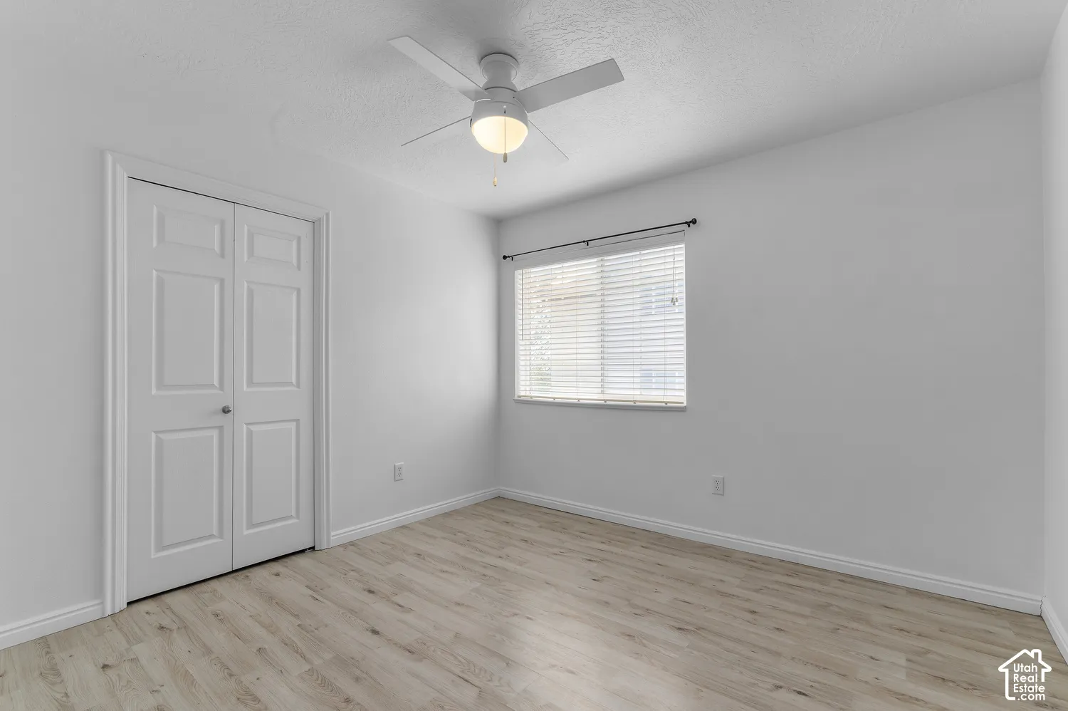 Interior space featuring wood-finish flooring, a ceiling fan with integrated lighting, dual-panel closet doors, and a window with horizontal blinds