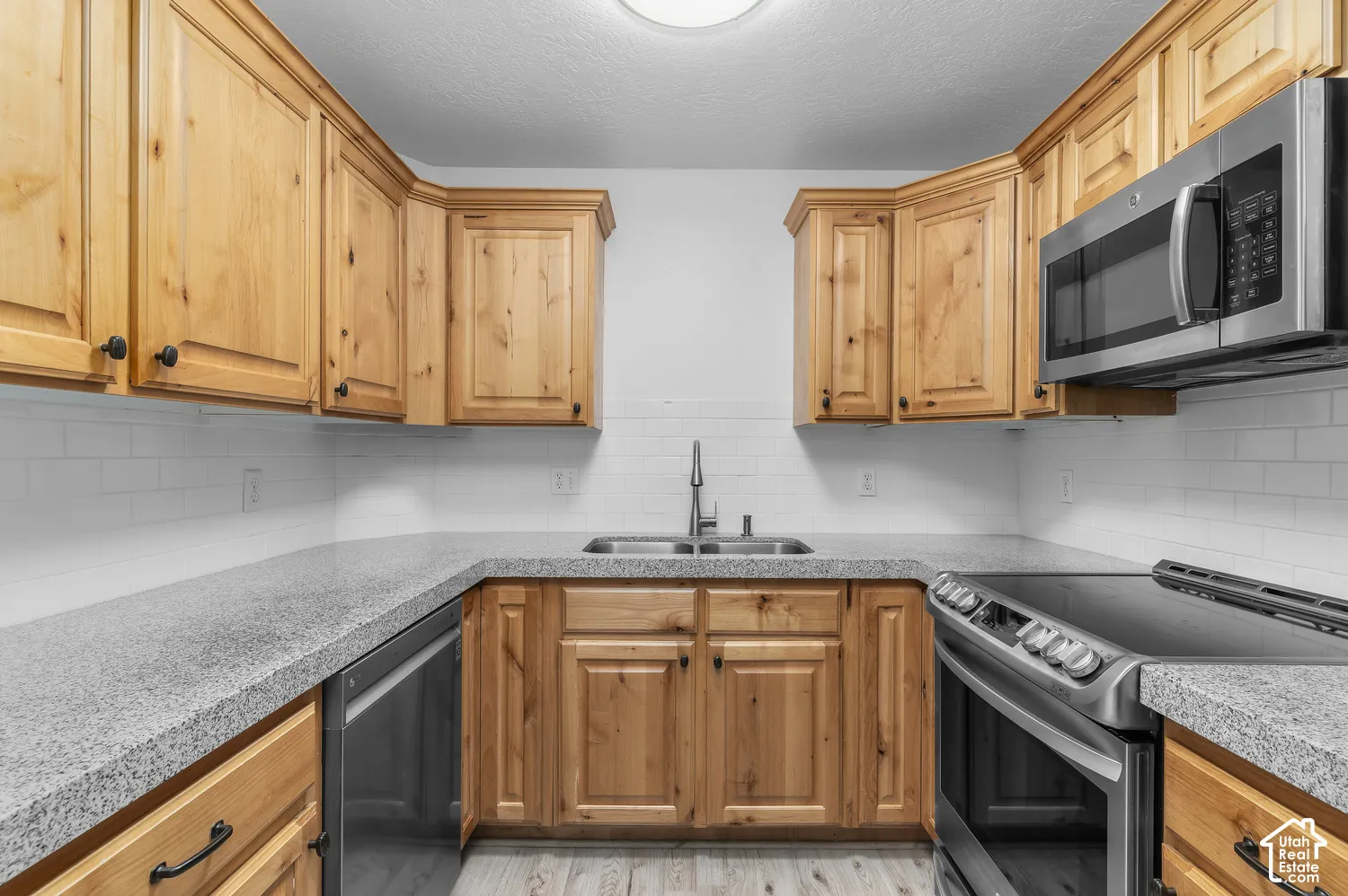 Kitchen featuring natural wood cabinetry, speckled countertops, stainless steel appliances, and white subway tile backsplash