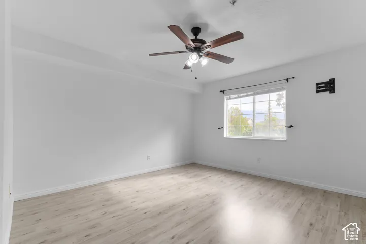 Light-filled room featuring wood-finish flooring, a ceiling fan with integrated lighting, and a window with exterior mullions