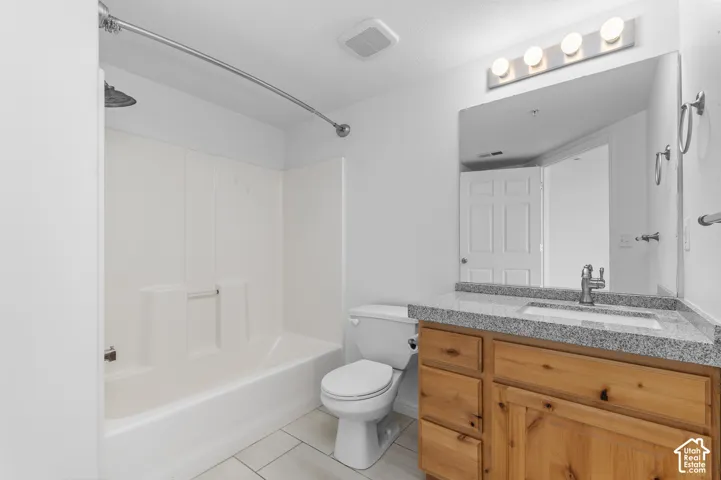 Bathroom featuring a wood-tone vanity, stone-finish countertop with an integrated rectangular sink, large wall-mounted mirror, four-bulb vanity light, and a white tub-shower combination
