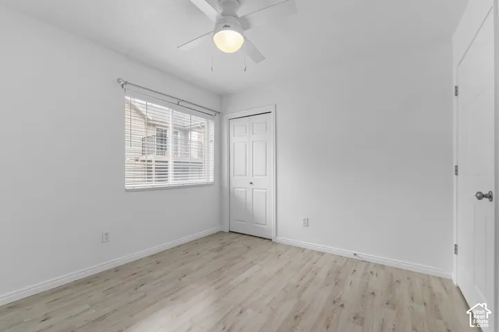 Neutral-toned wood-finish flooring, ceiling fan with integrated light fixture, horizontal window blinds, and paneled closet doors
