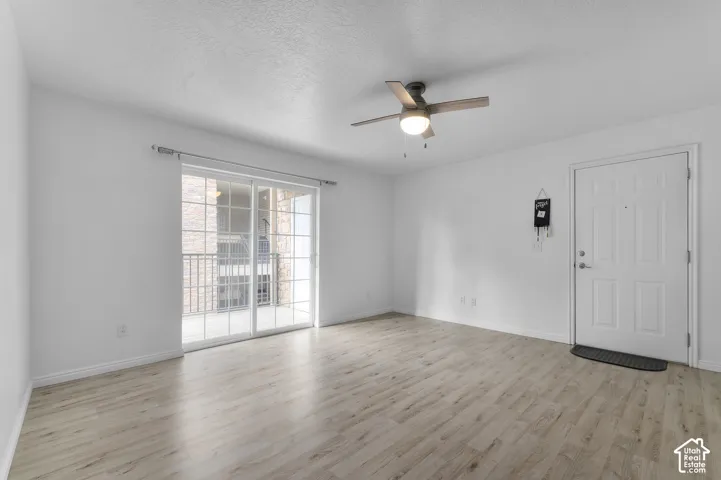 Light-filled interior space featuring wood-finish flooring, sliding glass doors, a ceiling fan with integrated lighting, and a paneled entry door