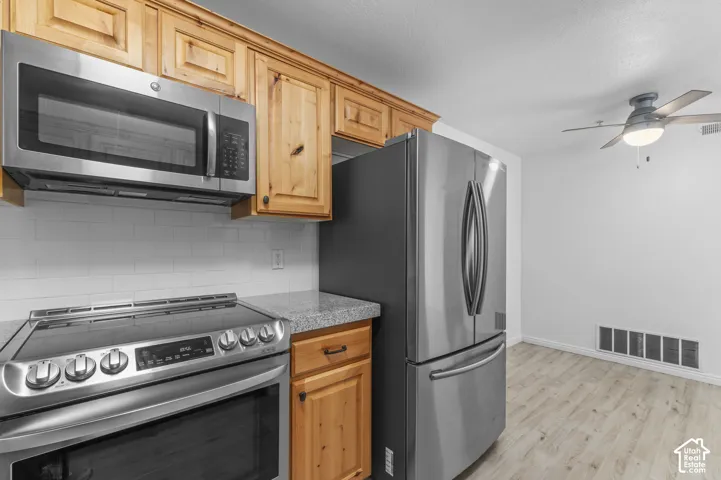 Kitchen featuring wood-finish cabinetry, stone-texture countertops, subway tile backsplash, stainless steel appliances, and wood-finish flooring
