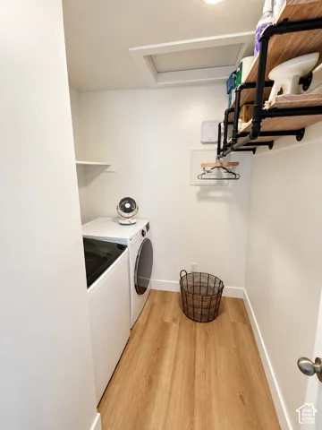 Laundry area featuring wood-finish flooring, built-in shelving with industrial-style black pipe supports, and an integrated hanging rod