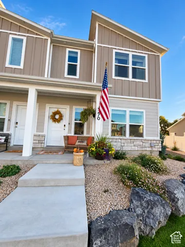 Multi-level residence featuring vertical board-and-batten siding, horizontal lap siding, stone veneer accents, covered front porch with square columns, and professional xeriscaping with decorative rock and boulders