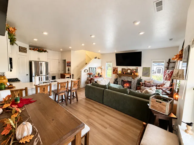 Open-concept floor plan featuring wood-finish flooring, recessed lighting, kitchen island with stone countertop, and a stone-surround fireplace with a timber mantel
