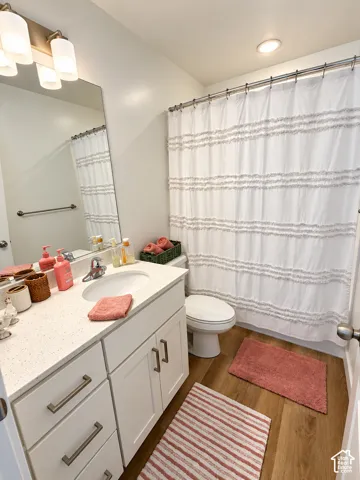 Bathroom featuring white cabinetry, solid surface countertop with an integrated basin, wood-finish flooring, and a multi-bulb vanity light fixture